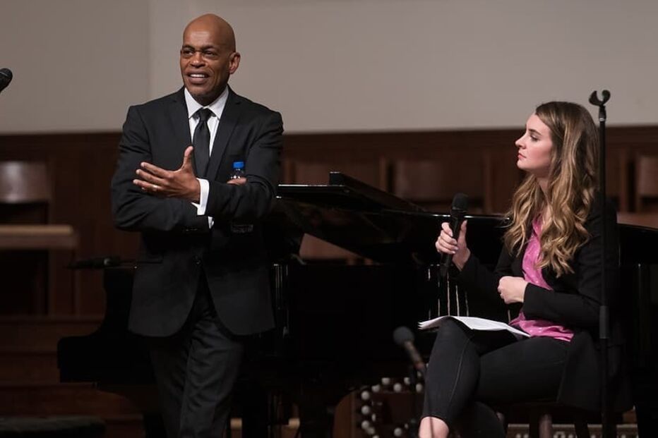 Um homem e uma mulher conversam com microfones em palco