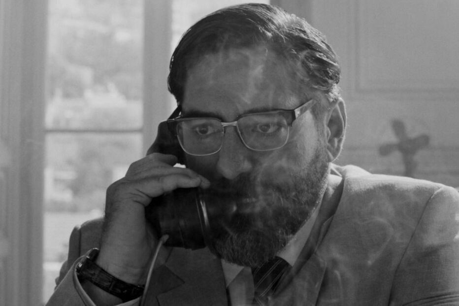 Homem ao telefone com óculos e barba, num filme a preto e branco