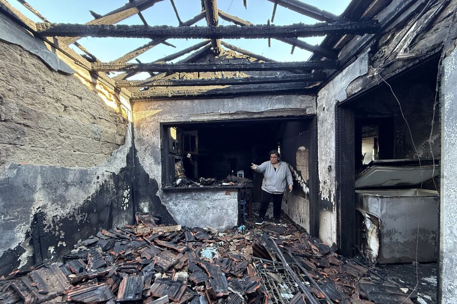 Casa destruída após incêndio, mulher observa os danos