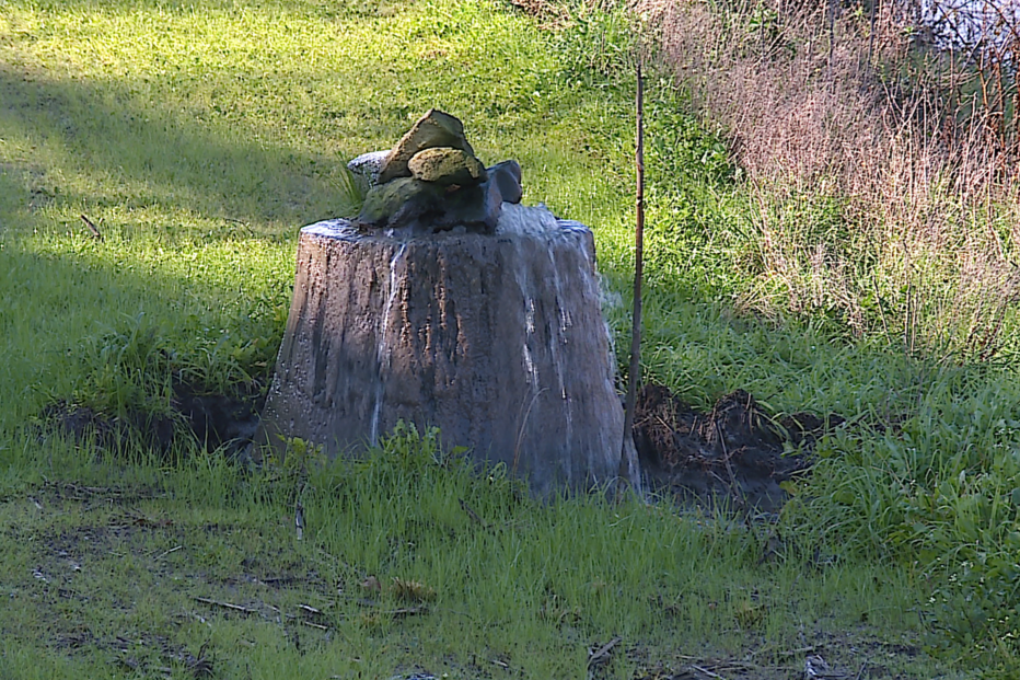 Cachoeira improvisada num tronco de árvore com pedras no topo, num jardim relvado