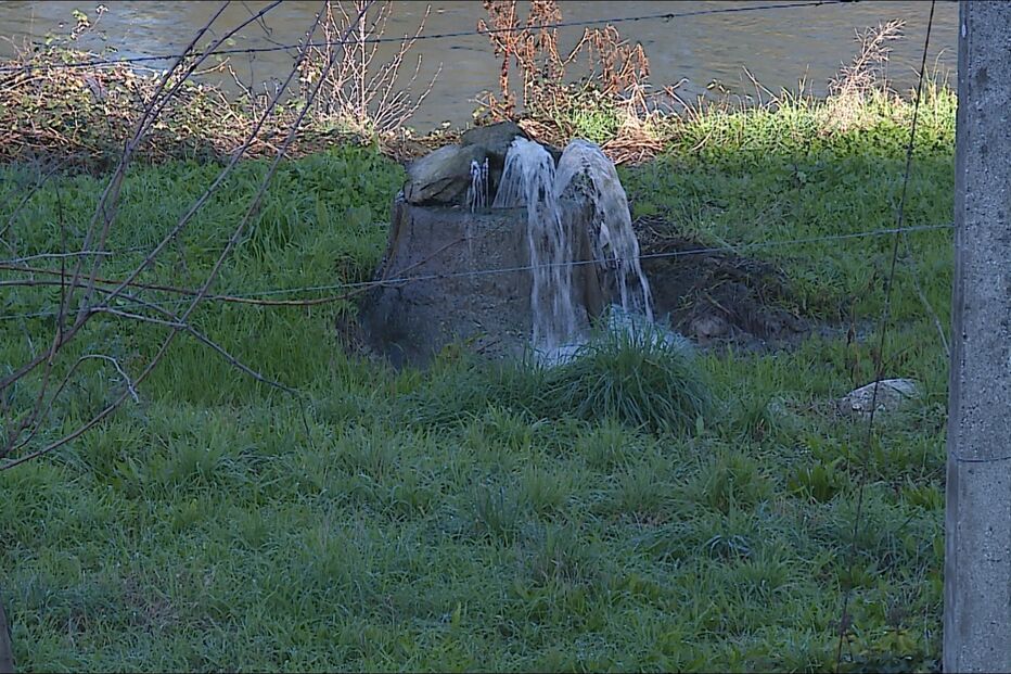 Água jorra de estrutura de pedra num campo relvado junto a um rio