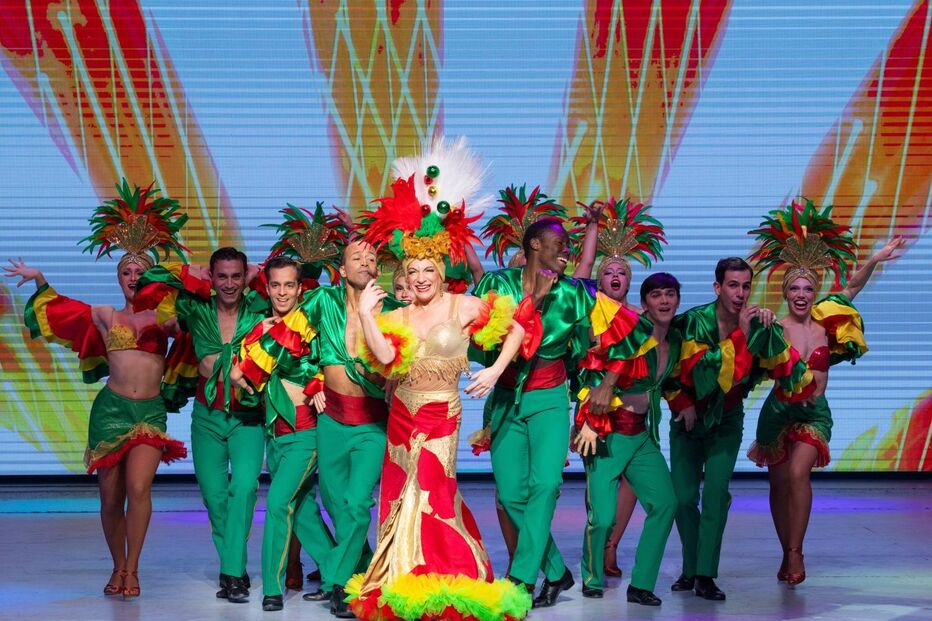 Grupo de artistas atua num palco com trajes vibrantes e coloridos