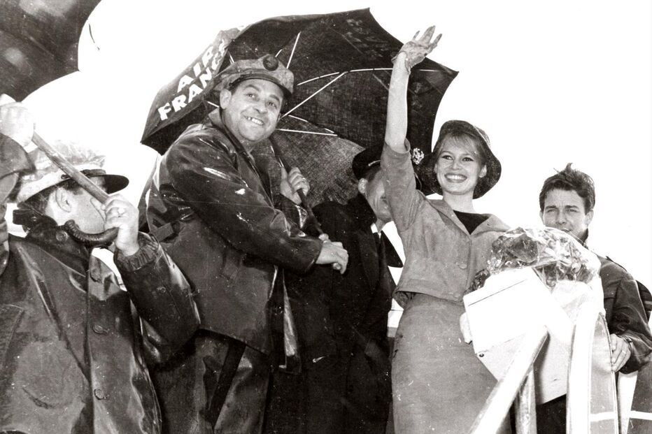 Brigitte Bardot sorri e acena num evento ao ar livre com fãs e fotógrafos