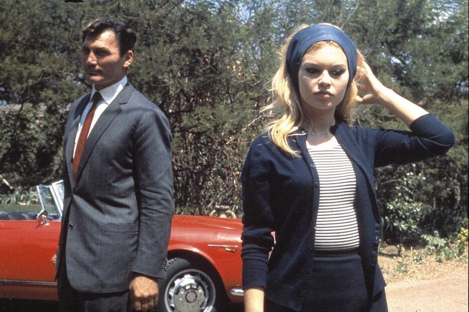 Brigitte Bardot e homem posam perto de carro vermelho