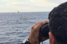 Homem usa binóculos para observar um barco no mar