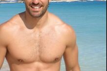 Homem sorri para a câmara numa praia com água azul cristalina