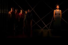 Espetáculo teatral aborda imigração com elenco diversificado e cenários minimalistas.

