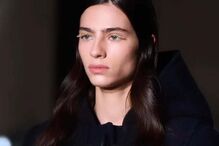 Modelo veste casaco com capuz e apresenta maquilhagem de pestanas douradas.
