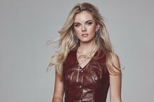 Mulher com colete de cabedal castanho e calças a combinar posa para a câmara