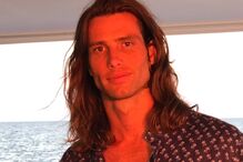 Um homem com cabelo comprido e camisa estampada num barco