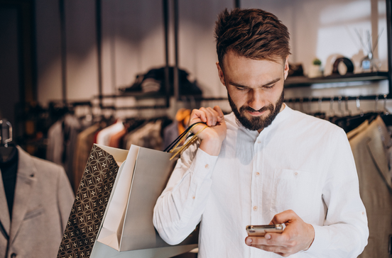 Homem com sacos de compras usa smartphone; ofertas do dia para um dia mais leve