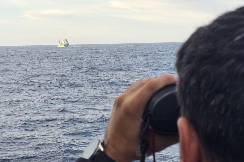 Homem usa binóculos para observar um barco no mar