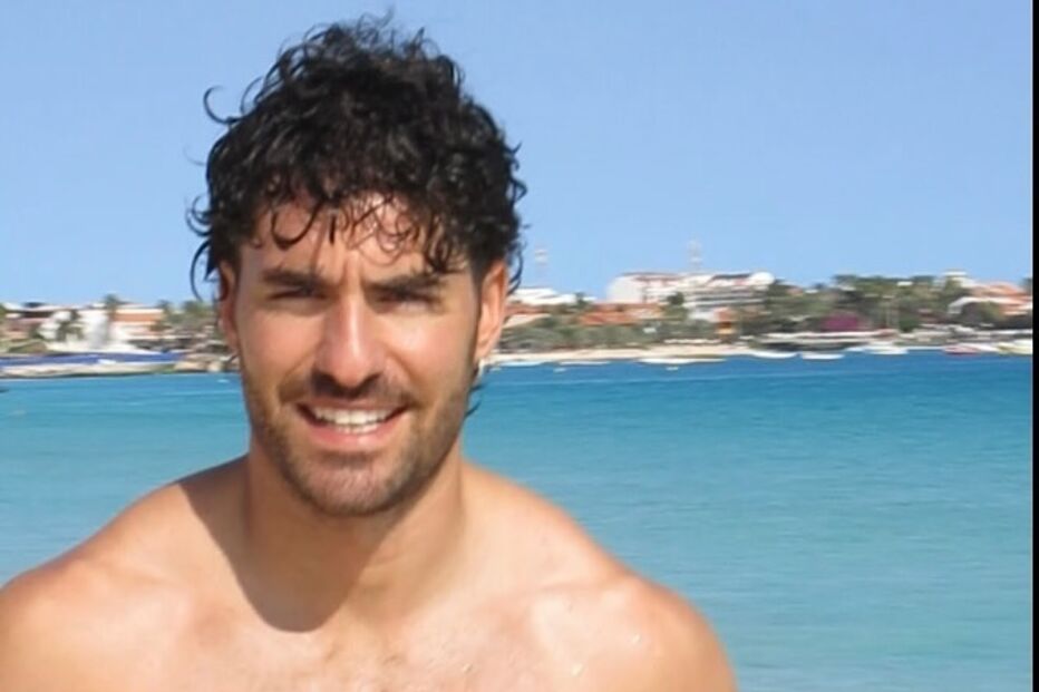 Homem sorri para a câmara numa praia com água azul cristalina