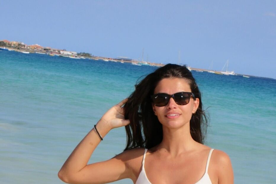 Mulher de biquíni branco e óculos de sol relaxa numa praia de areia clara