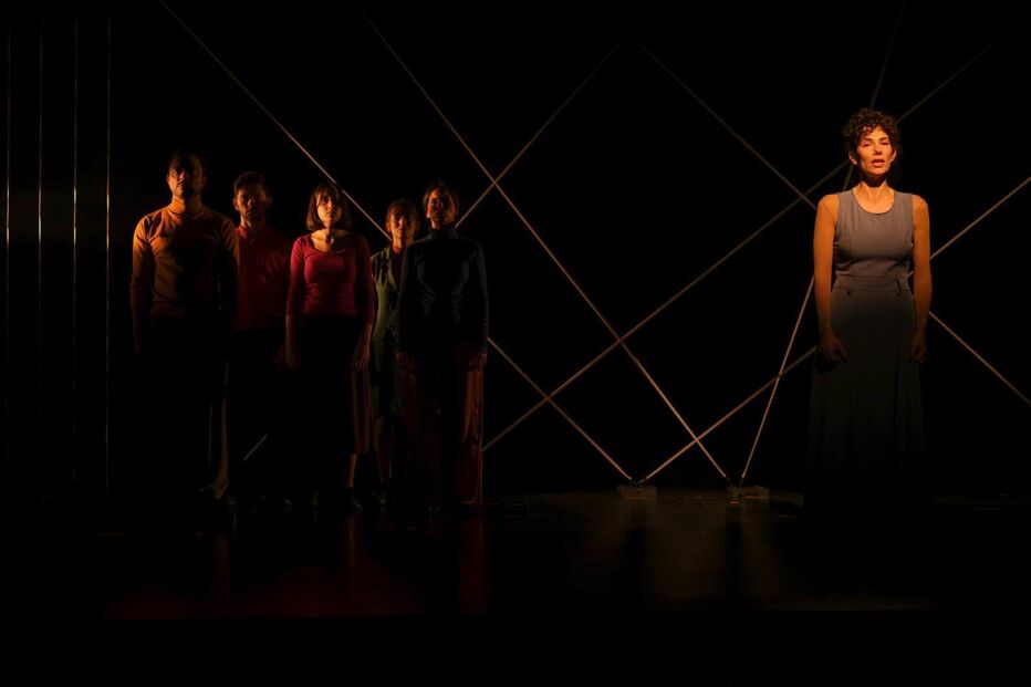 Espetáculo teatral aborda imigração com elenco diversificado e cenários minimalistas.
