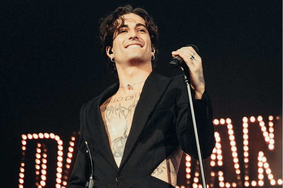 Damiano David atua no palco com um fato preto e microfone