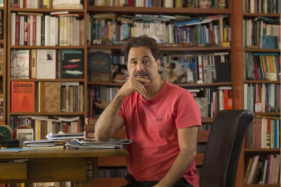 Homem posa junto a uma estante de livros