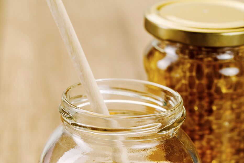 Dois frascos de vidro com mel e uma colher de madeira num deles