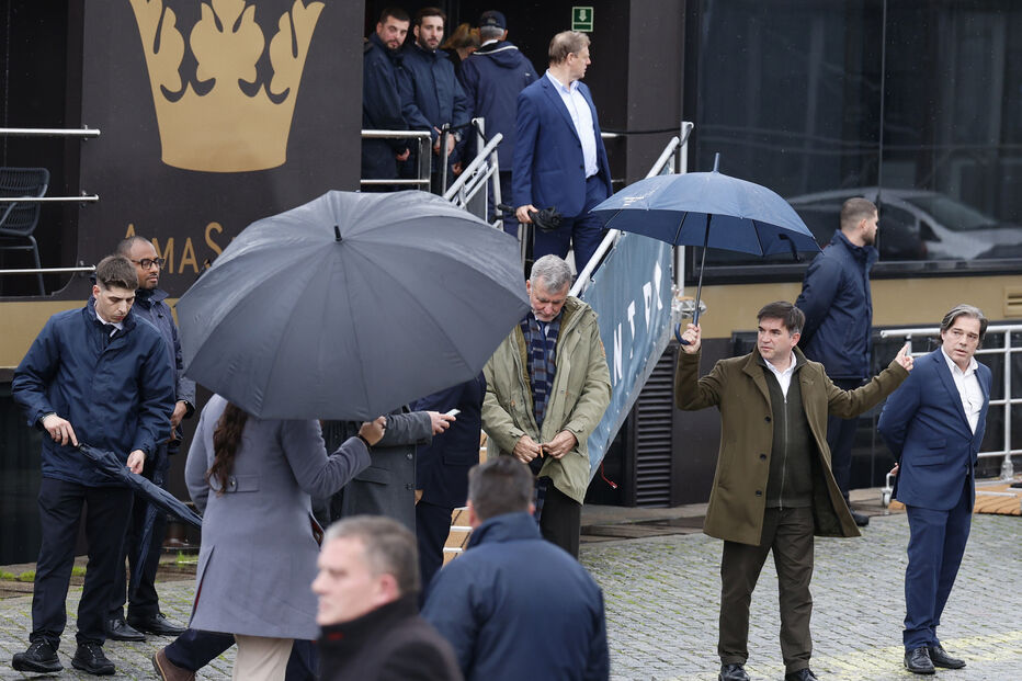 Pessoas caminham à chuva com guarda-chuvas em frente a um edifício