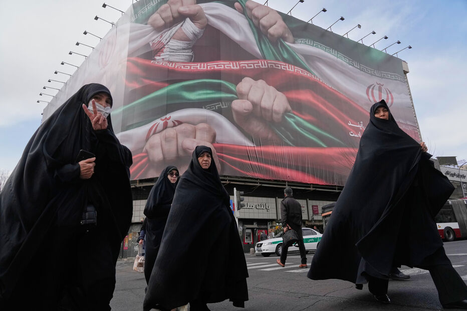 Mulheres iranianas caminham perto de cartaz com a bandeira do Irão, em Teerão