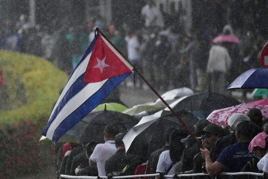 Militares cubanos em evento sob chuva com a bandeira de Cuba