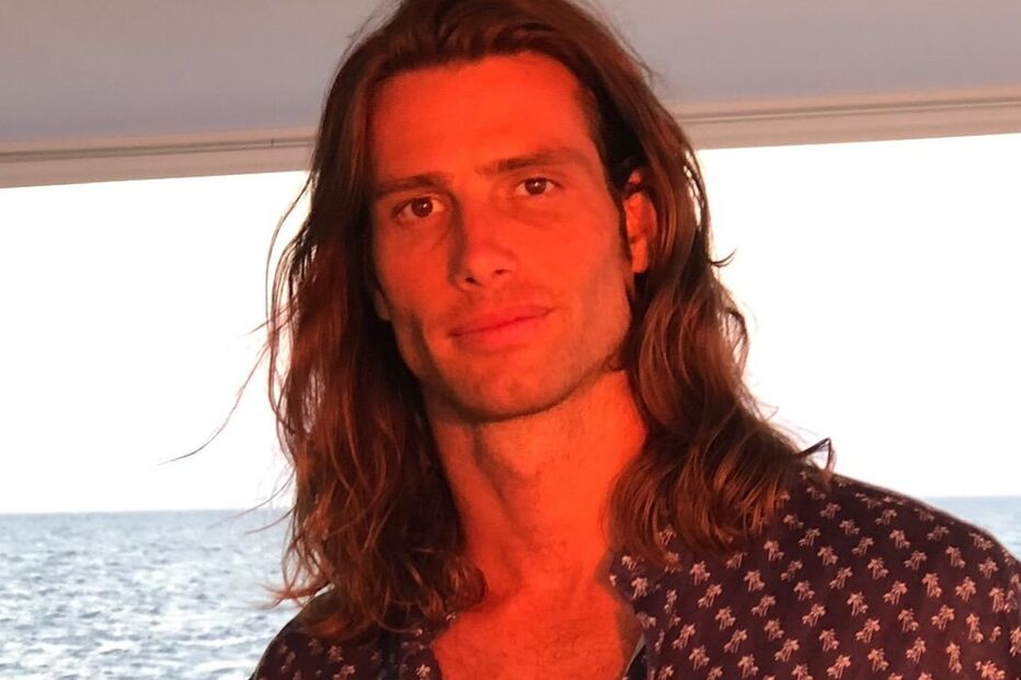 Um homem com cabelo comprido e camisa estampada num barco