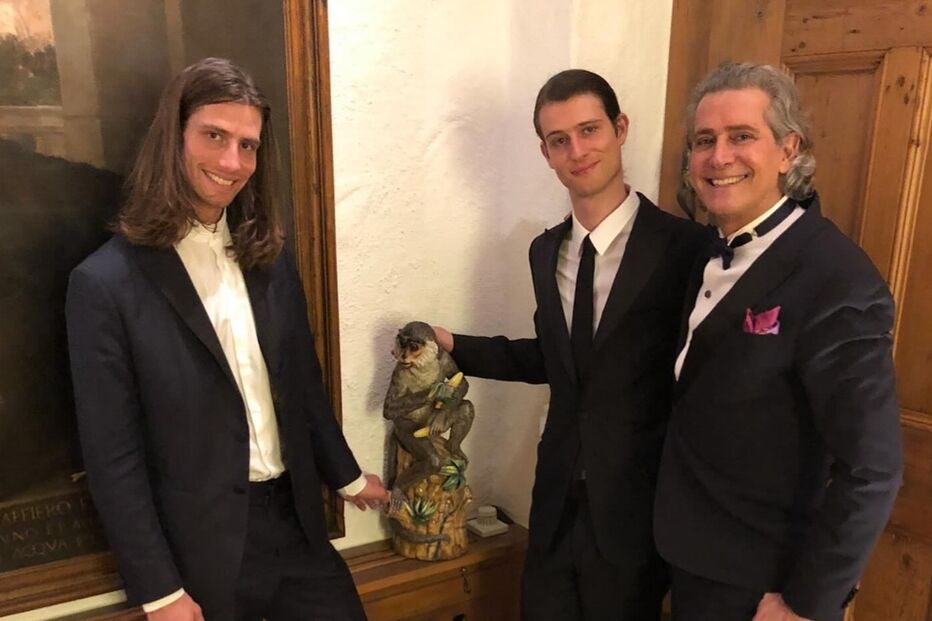 Três homens de fato posam junto a uma estátua de macaco