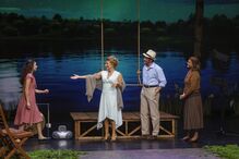 Espetáculo teatral com atores em palco e cenário de lago