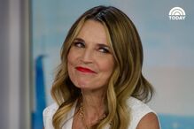 Mulher sorri com batom vermelho, colar dourado e vestido branco