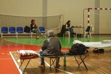 Pessoas aguardam em espaço que aparenta ser um abrigo temporário