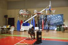 Homem amarra sapatos perto de aquecedor num ginásio com tabelas de basquetebol