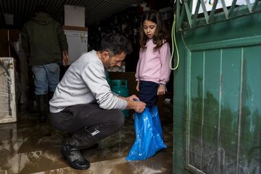 Um homem coloca plásticos nos pés da filha para proteger da chuva, numa zona inundada na zona ribeirinha de Alcácer do Sal, Setúbal.