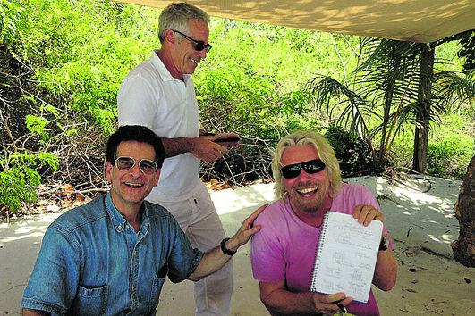 Richard Branson sorri com um bloco de notas ao lado de duas pessoas