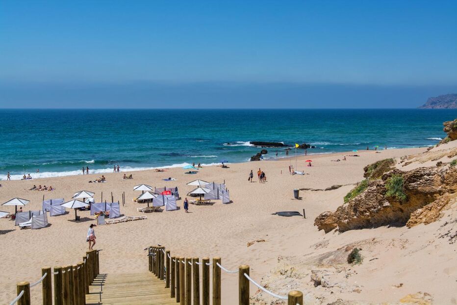 Praia da Comporta com pessoas, mar e passadiço de madeira em dia soalheiro