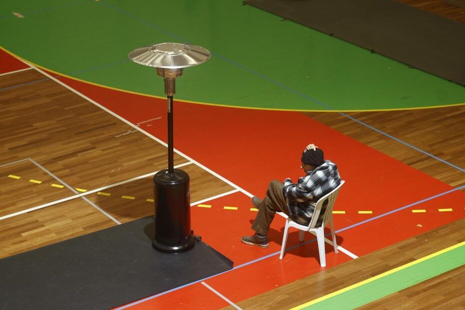 Homem senta-se perto de aquecedor num campo desportivo interior