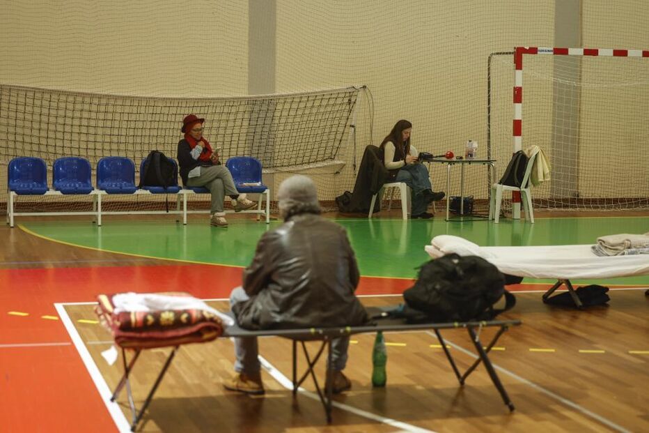 Pessoas aguardam em espaço que aparenta ser um abrigo temporário