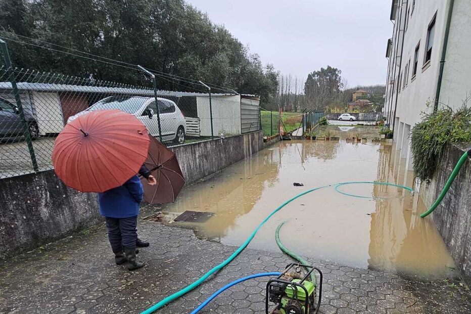 Inundação perto de habitações, pessoa com guarda-chuva observa a água