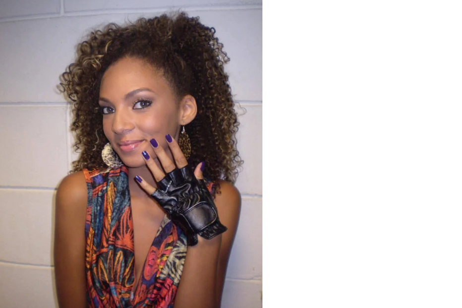 Mulher sorri com unhas pintadas, roupa colorida e uma luva preta