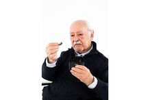 Idoso examina aparelho auditivo Philips, promovendo cuidado com a audição