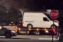 Uma carrinha branca danificada em cima de um reboque na rua