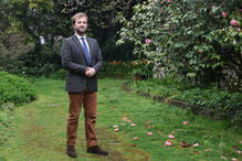 Homem posa num jardim com camélias em flor