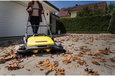 Mulher usa máquina de varrer folhas no jardim de uma casa