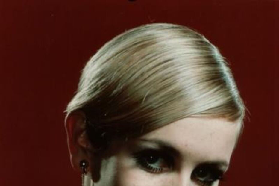 Twiggy sorri com grandes brincos dourados e um penteado elegante