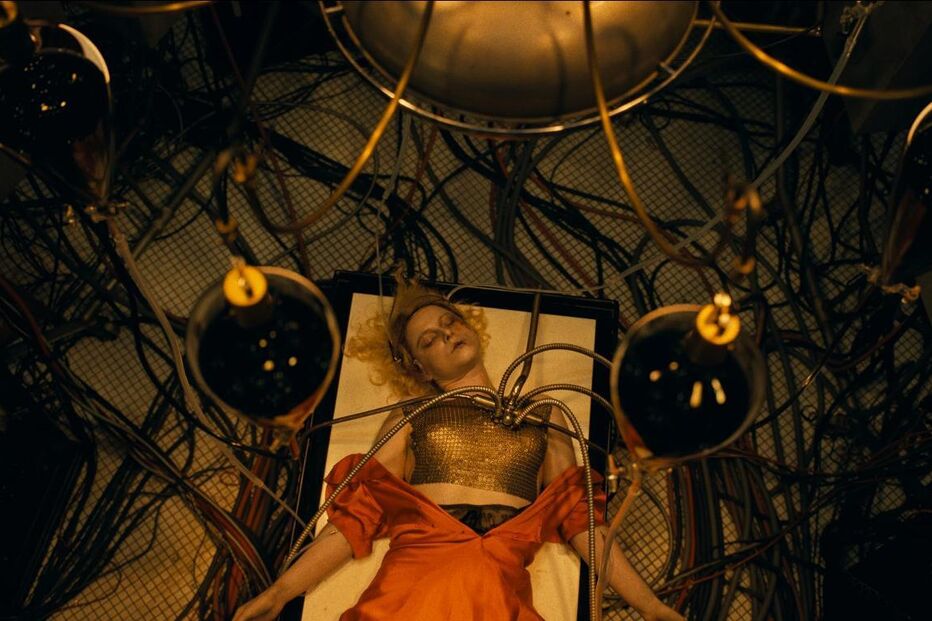 Mulher deitada, ligada a cabos, num cenário que evoca ficção científica ou fantasia