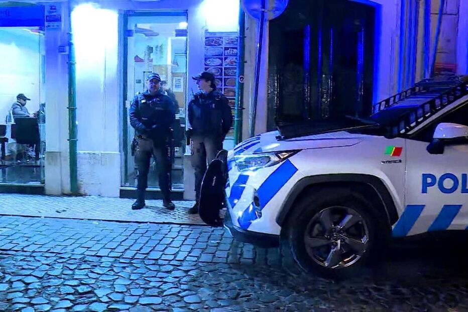 Polícias perto de restaurante à noite com carro da polícia em primeiro plano