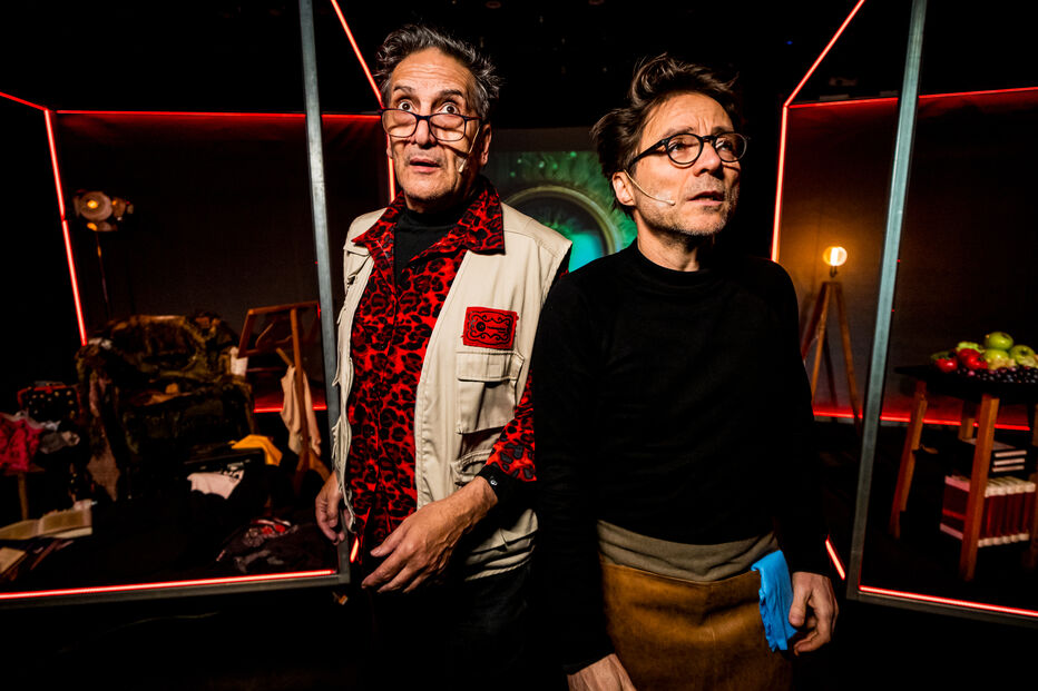 Dois homens em palco sob luzes vermelhas preparam-se para atuar