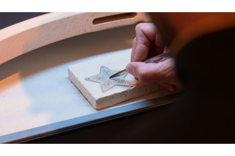 Homem trabalha numa estrela de prata com pinças