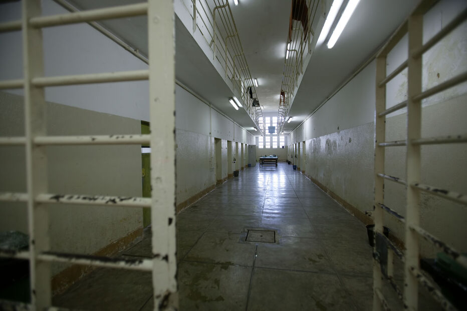 Corredor prisional com celas e grades, onde reclusos cumprem penas longas