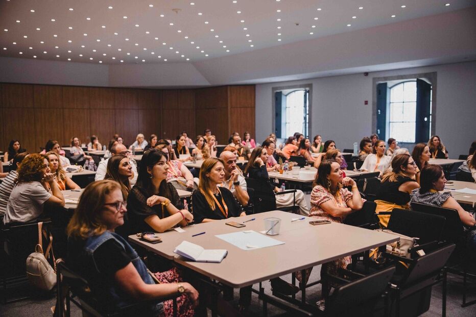 Pessoas assistem a uma apresentação numa sala com mesas e cadeiras