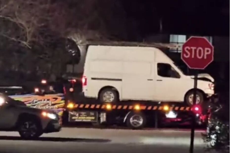 Uma carrinha branca danificada em cima de um reboque na rua